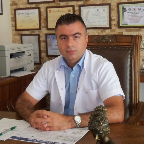Kliniğimizden görüntü: Op. Dr. Murat Ataseven muayene masasında, beyaz önlük; arkada çerçeveli sertifikalar (klinik ofisi)